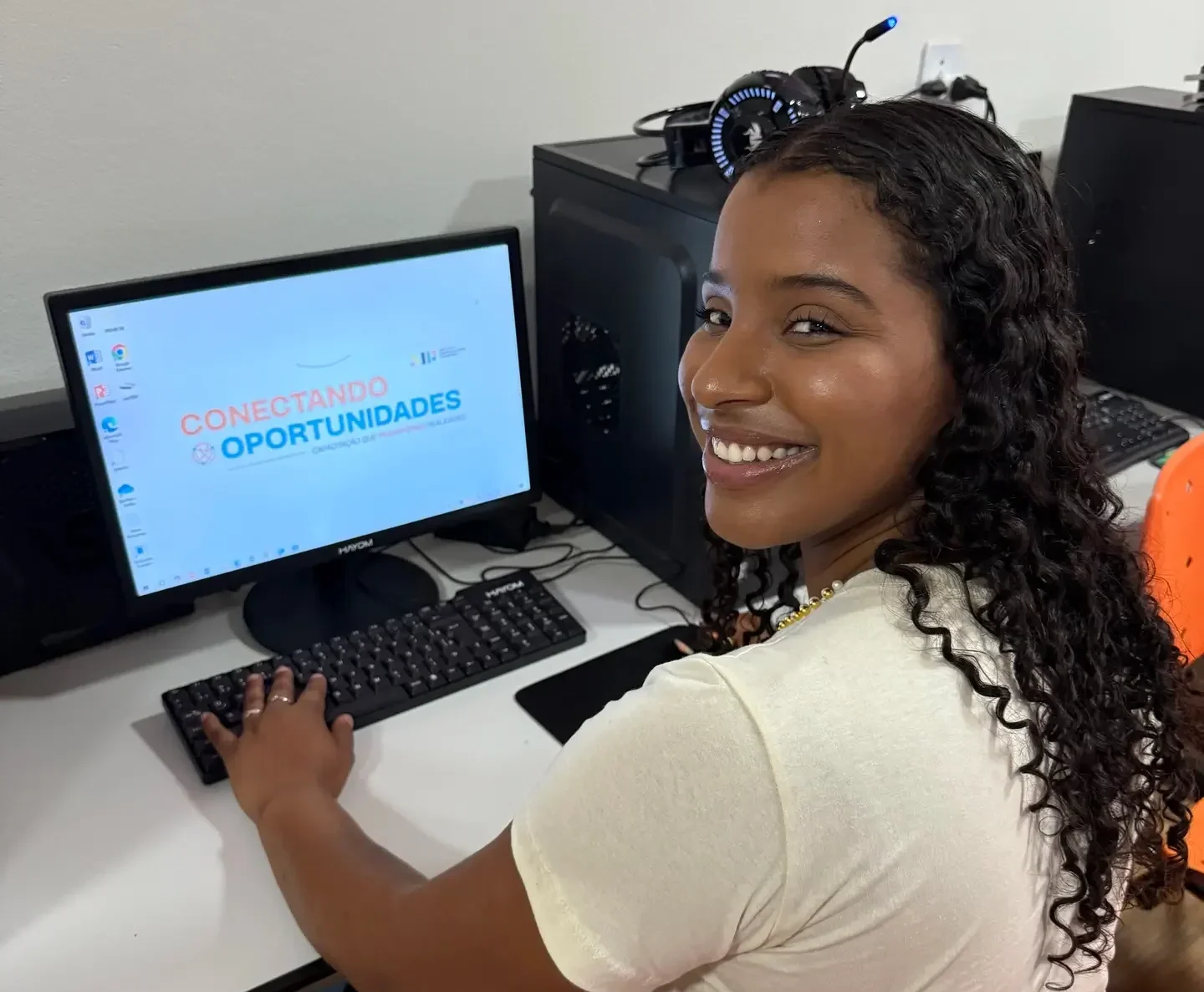 Aluna do projeto social Conectar Oportunidades dentro de sala de aula digitando no computador e sorrindo para a foto