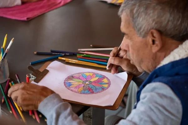 Senhor do projeto social ASSOPOC desenhando em uma prancheta com alguns lápis espalhados