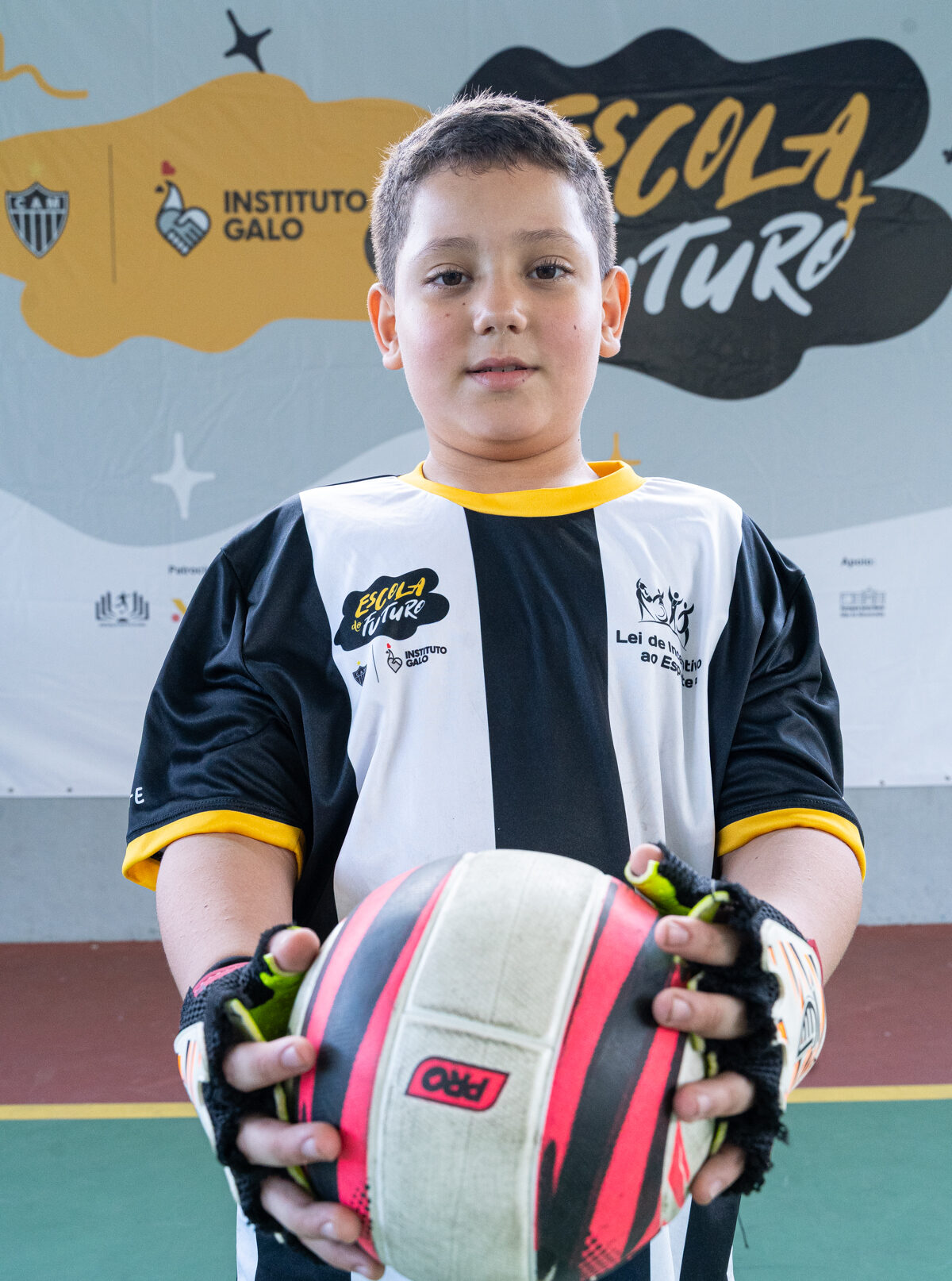 Aluno sorridente do projeto social Escola do Futuro do Instituto Galo com camisa de time de futebol e segurando uma bola