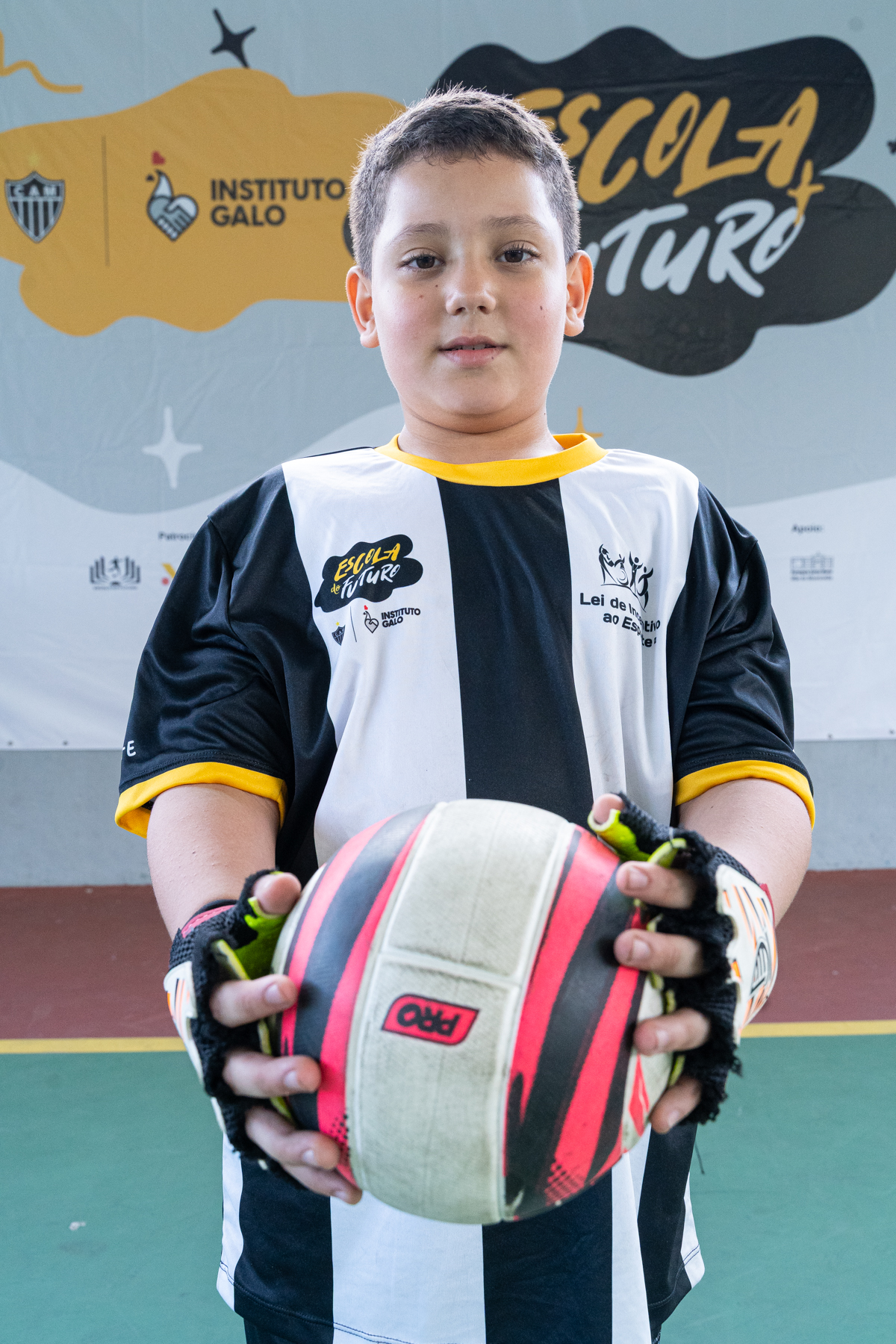 Aluno sorridente do projeto social Escola do Futuro do Instituto Galo com camisa de time de futebol e segurando uma bola