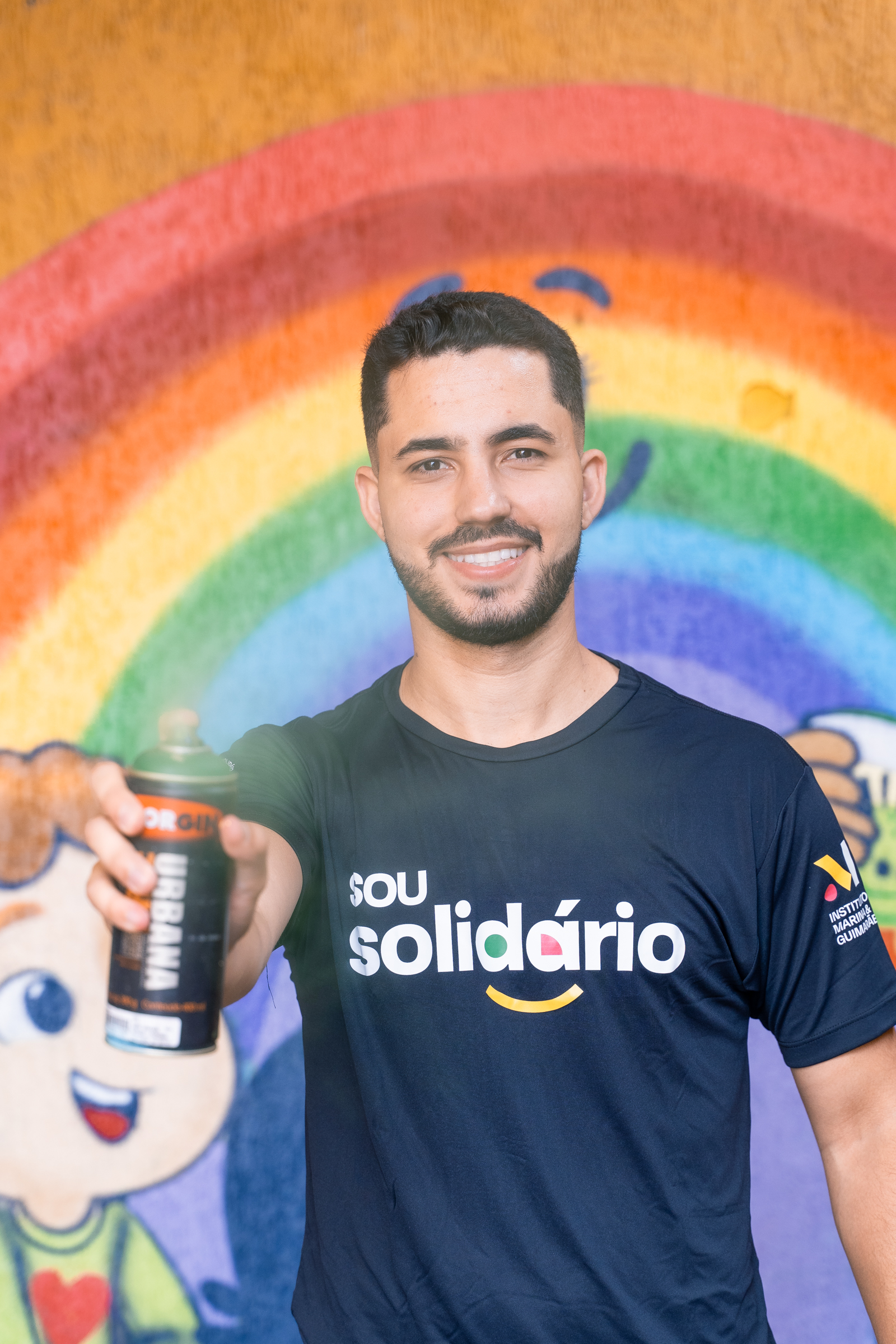 Voluntário sorridente do projeto social MF Solidário com o spray de tinta apontando para a câmera