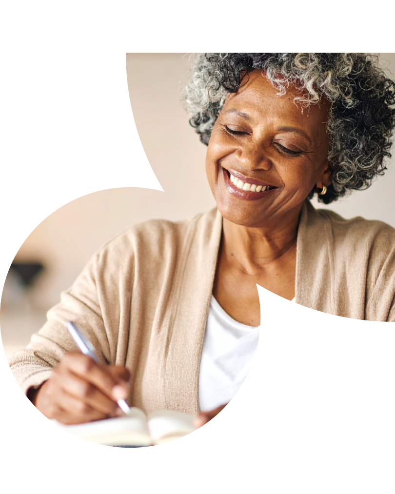 Mulher 50+, negra, com cabelos cacheados curtos, escrevendo em um caderno.